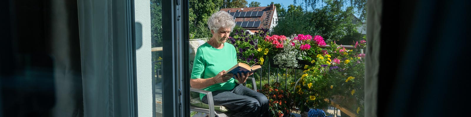 Spendenseite-20240812-ricam-orchideenweg-gäste-6 Bewohnerin des Ricam Hospizes sitzt mit einem Buch auf ihrem Balkon